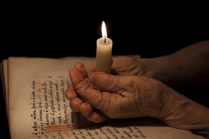 old hands holding candle over Bible