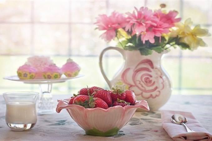 table with bowl of strawberrys glass of milk and vase