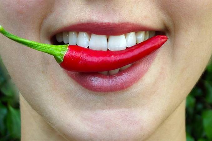 a womans mouth biting a hot pepper