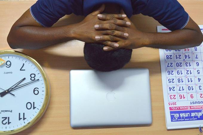 A man bows his head on a table near the clock and a calendar