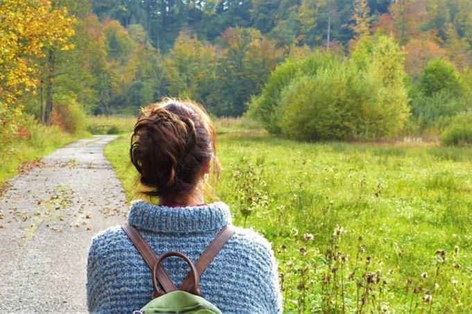 the back of a woman holding a backpack on a trail