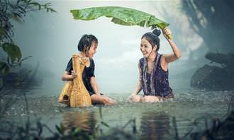 two women in a river using a big leaf as shelter from the rain