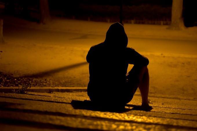 the back of a hood man sitting on a sidewalk at night