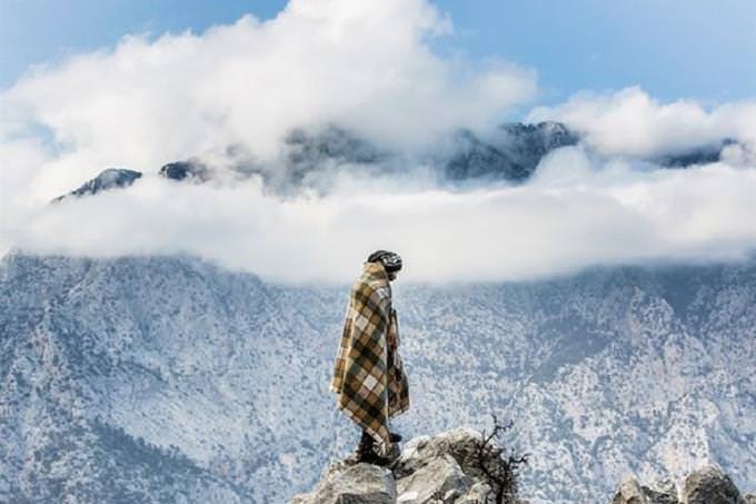 man in blanket standing in front of snowy mountain