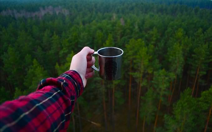 holding coffee above woods