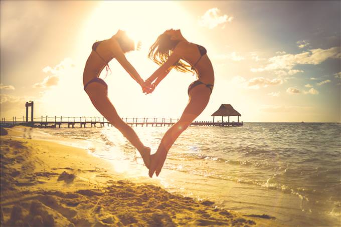 girls making heart sign at beach