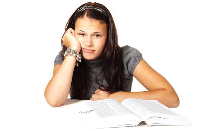 A woman looking upset and sitting in front of a book with her head in her hand