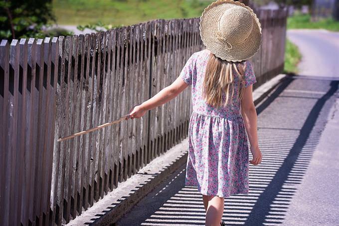 A girl walking beside a fence with a stick in her hand