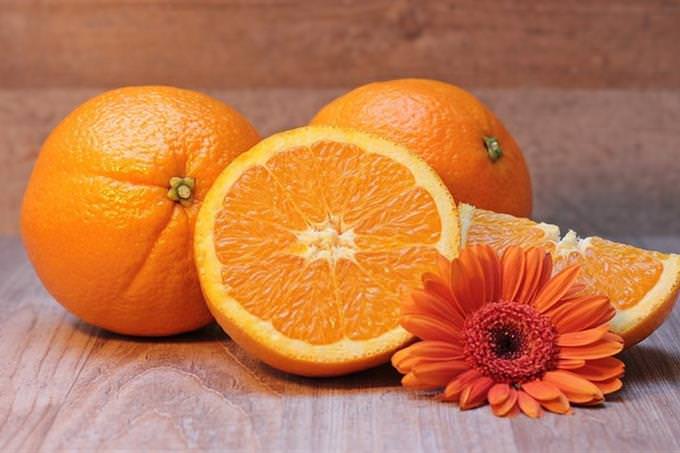 Three oranges with one cut in half and an orange flower next to them