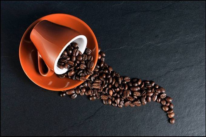 a cup of coffee on its side and coffee beans pouring out of it