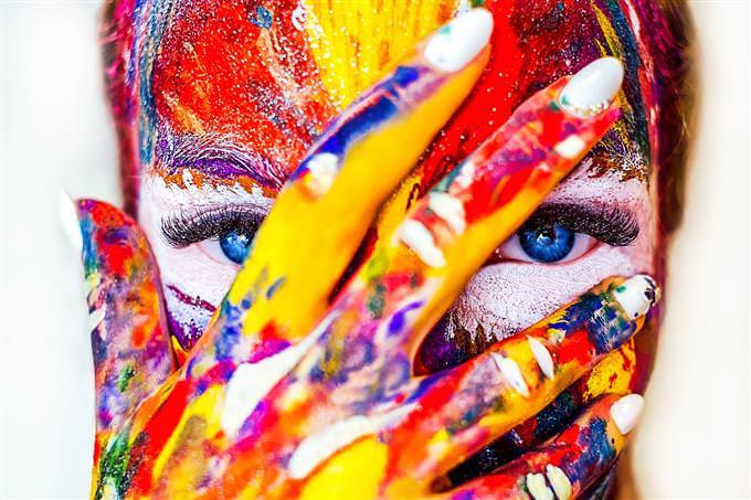 A woman covered in color hiding her face with her hand