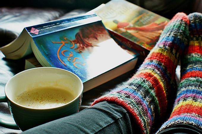 A woman's legs with wool socks, and a book and a hot drink next to them