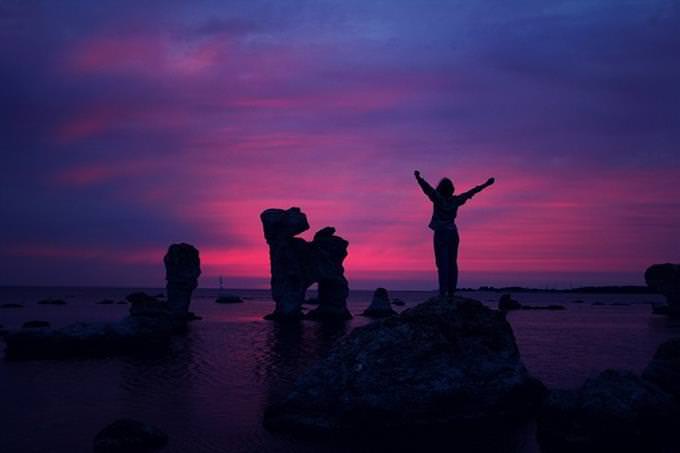 A woman standing on a rock in the sea at dusk