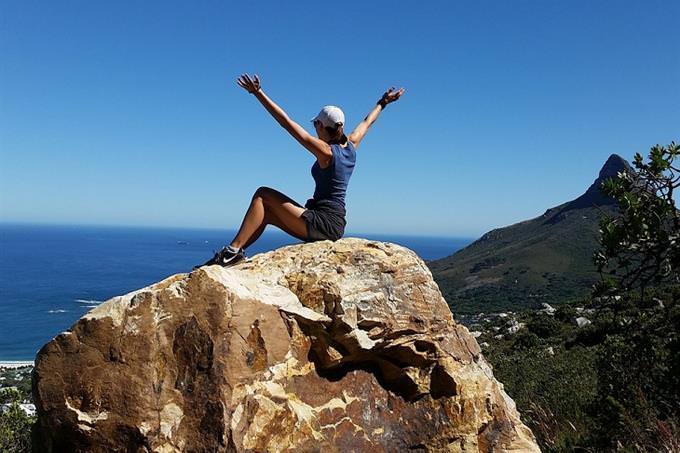 A woman sitting on a huge rock waving her hands