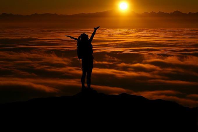 A woman standing on a cliff and waving her hands in the air during sunset