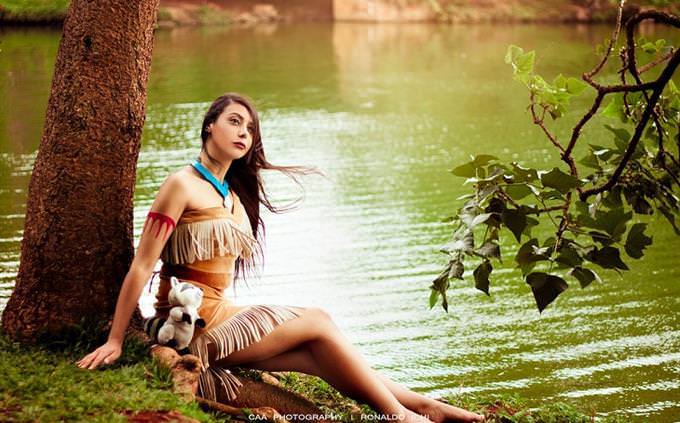 A woman dressed up as a Pocahontas sitting on the edge of a river