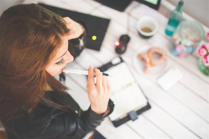 A woman sitting over a notebook with a pen in her mouth