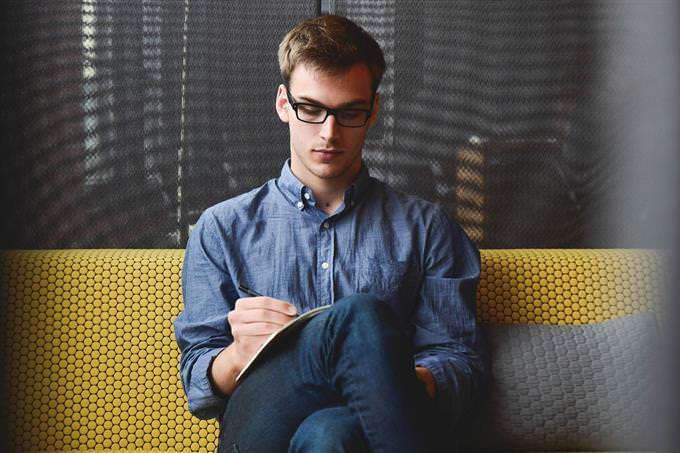 A man sitting on a sofa and writing in a notebook