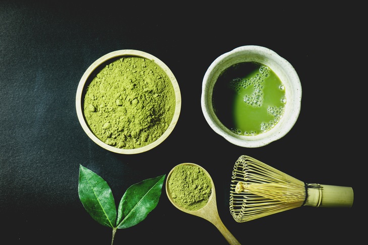 matcha powder, tea leaves, a cup of matcha, a matcha whisk and a spoonful of matcha