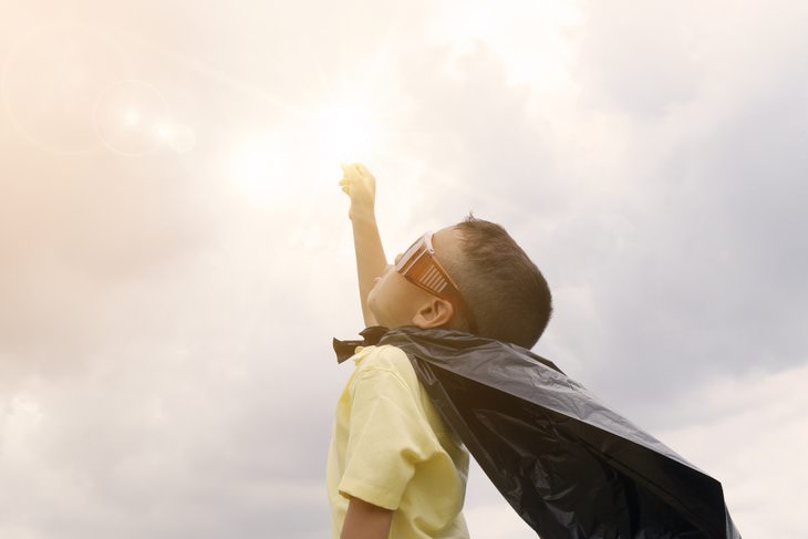 boy in glasses and a cape reaching for the Sun