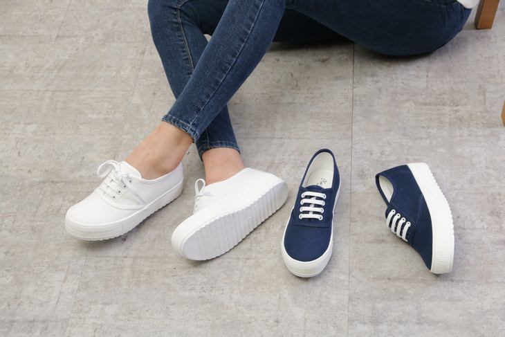 a woman in white tennis shoes is sitting next to a pair of dark blue tennis shoes