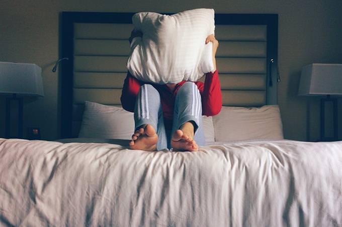 A woman sitting on the bed and covering her face with a pillow