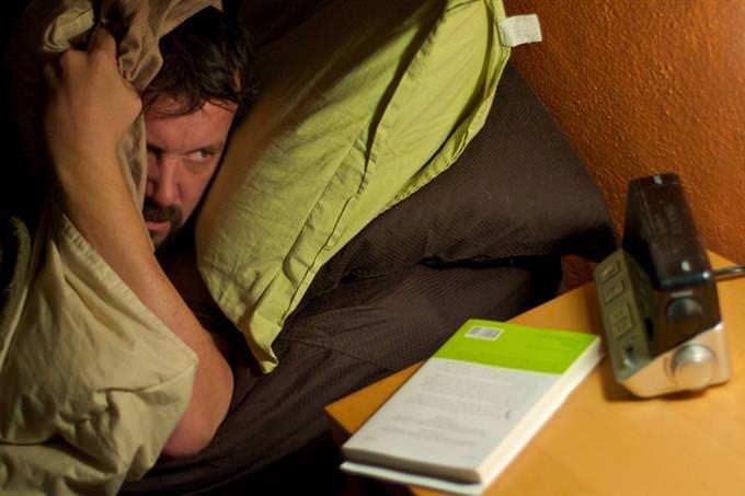A man peeking at an alarm clock from his bed
