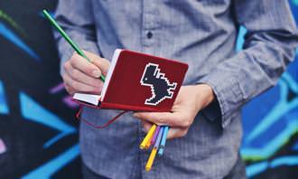 Find the differences: A man holding a notebook and colored pencils