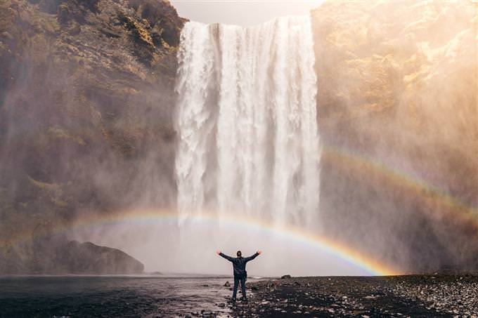 How your life flows: a man standing in front of a waterfall with his hands in the air