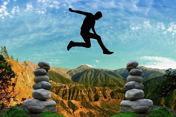 man jumping between two balanced rock piles