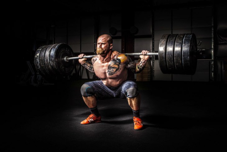 crouching bodybuilder with tattoos lifts big weight 