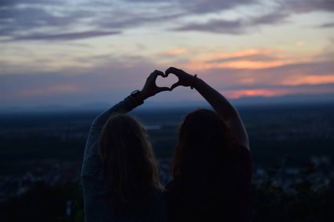 Two friends form a heart shape with their hands