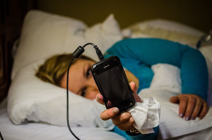 woman in bed looking at her charging cellphone