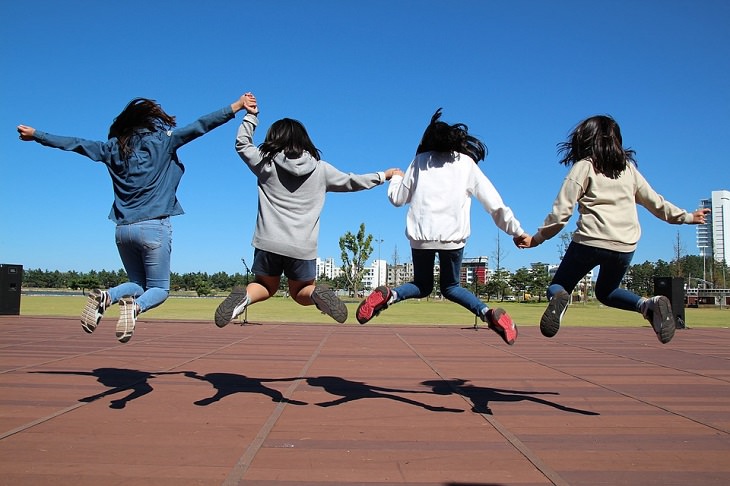 The back of a line of girls holding hands and jumping in the air