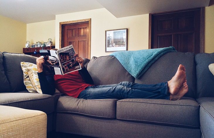 man laying on a couch reading a magazine