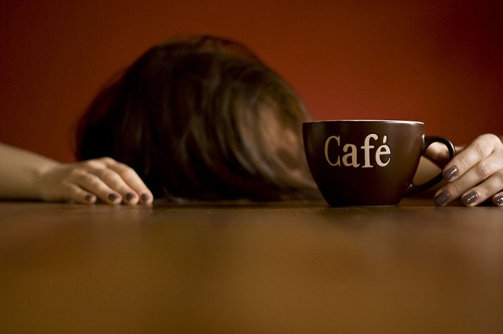 woman with her head down on the table holding a cup of coffee