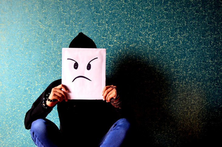 man holding a paper infront of his face with an angry face drawn on it