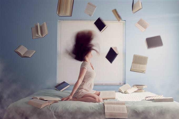A woman sitting on her bed throwing books around