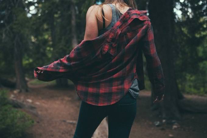 A woman standing in the forest holding her shirt