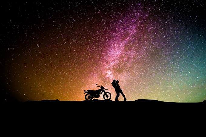 A couple hugging next t0 a motorbike with a starry sky in the background