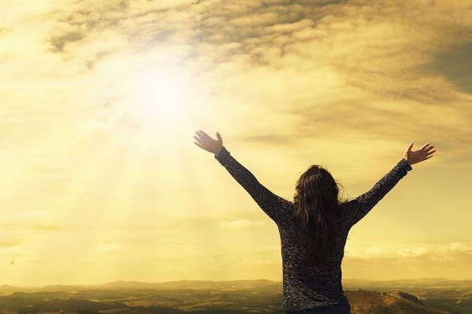 A woman opening her hands in front of the rising sun