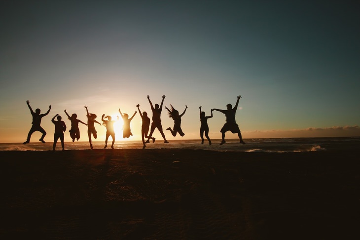 a group of people are jumping on a beach with the sun in the background