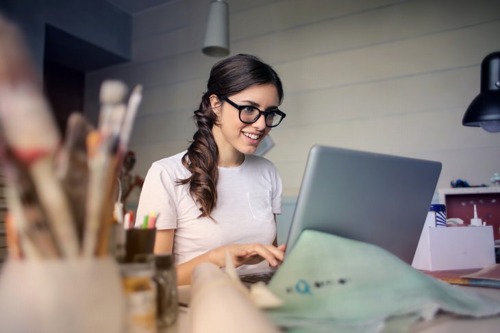 a woman wearing glasses is smiling as she is working at the laptop