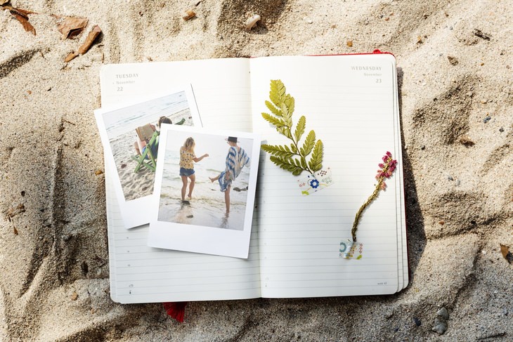 a journal with pictures and dried herbs laying on the beach