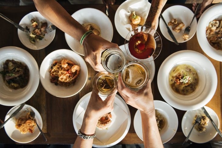 4 people join glasses with platefuls of food in the background