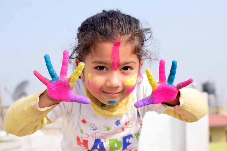 a girl is covered in colorful paint is showing her hands