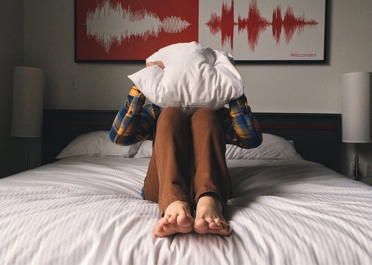 a man covers his head with a pillow while sitting on a bed