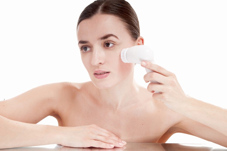 a woman using a cleansing face brush