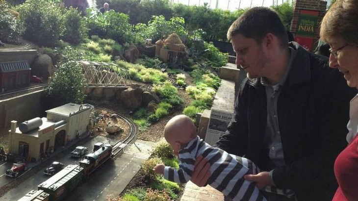 optical illusions man holding a baby above model train installation