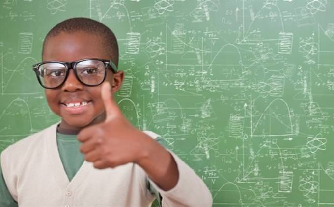 boy with glasses in front of a blackboard gives thumbs up